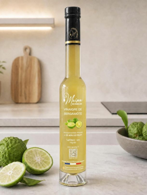 Bouteille de vinaigre de bergamote La Maison Des Grands Lacs entourée de bergamotes sur un plan de travail